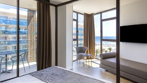 Une chambre d’hôtel moderne dotée d’un grand lit, d’une télévision à écran plat, d’un balcon offrant une vue sur la ville et d’un coin salon avec une chaise et une table.