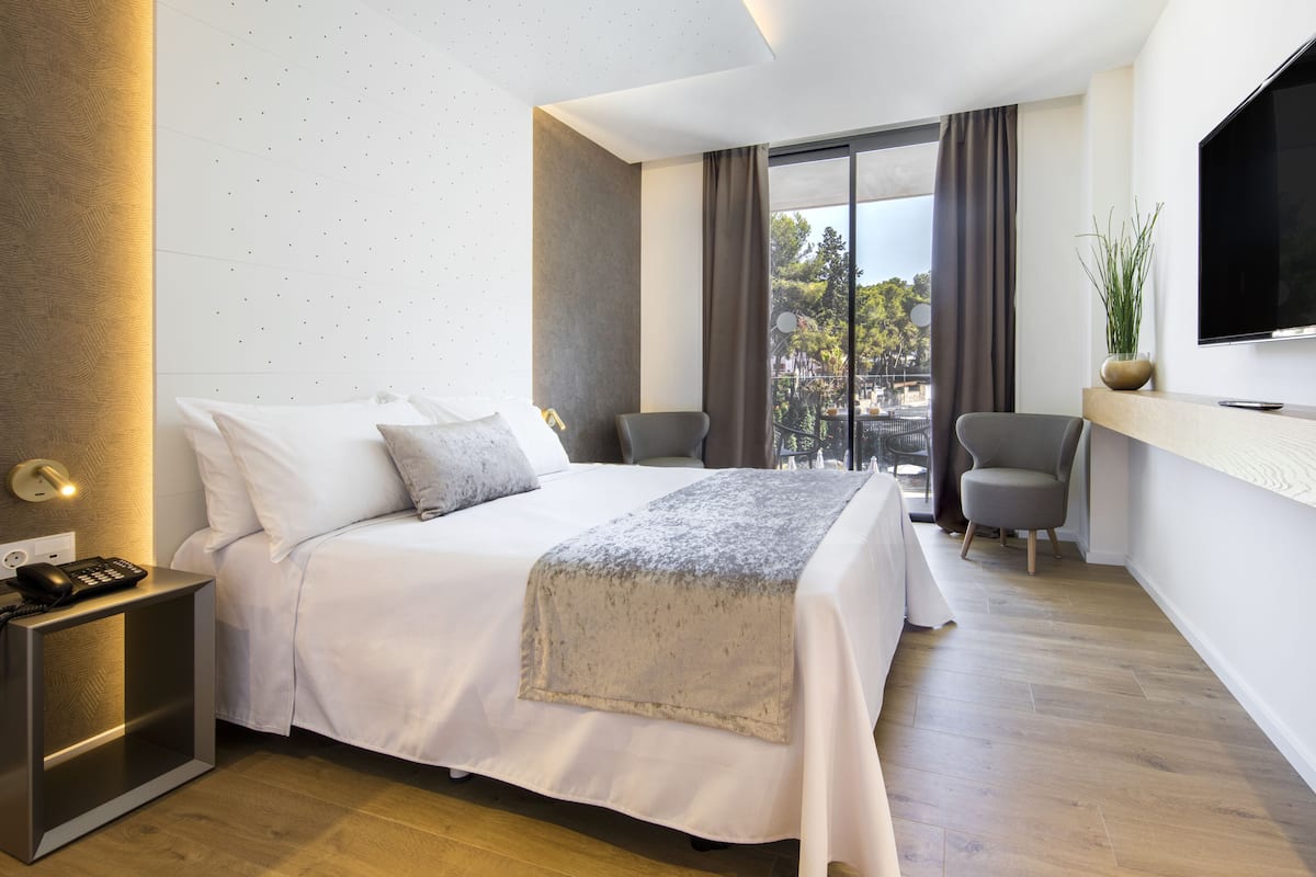Une chambre d’hôtel moderne dotée d’un grand lit, d’un bureau, d’une chaise, d’une télévision et d’un balcon avec vue.