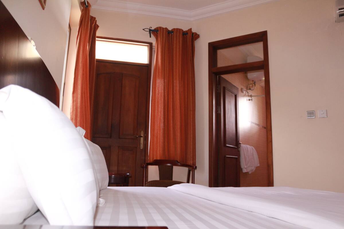 A hotel room with a bed, a chair, a wooden door, and a window with curtains.