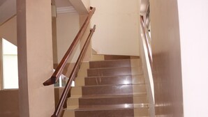 A staircase with wooden handrails and beige walls. - Windy Bay Guest House (Winneba)