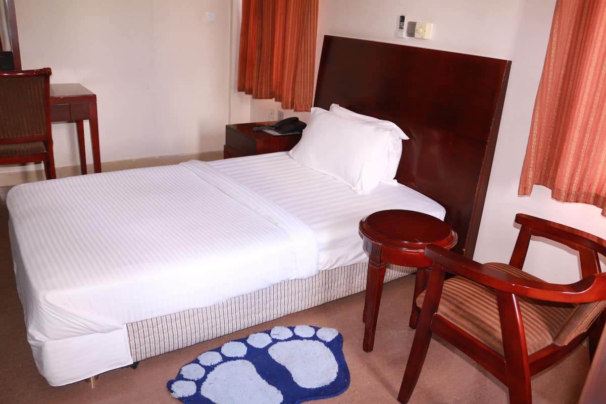 A hotel room with a large bed, a wooden nightstand, a chair, a desk, and a blue pet paw print rug.