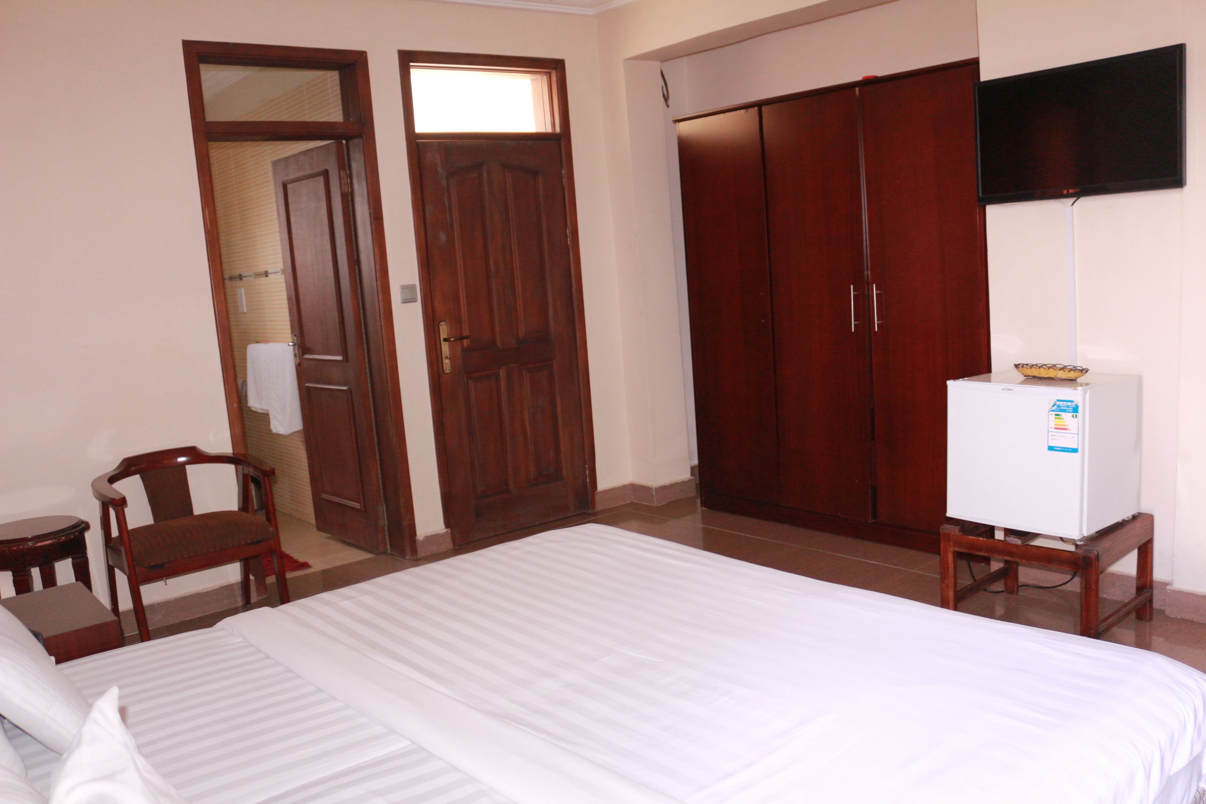Une chambre d’hôtel avec un lit, une armoire en bois, un téléviseur posé sur un meuble et une petite table.