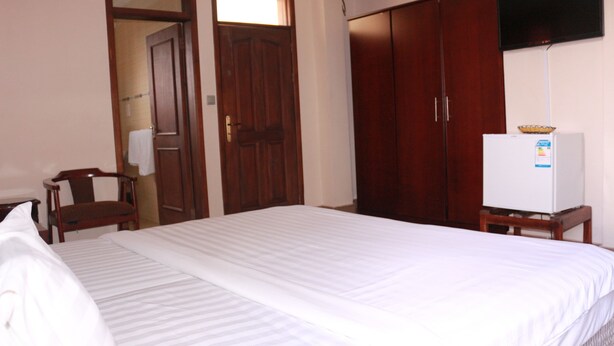 A hotel room with a large bed, wooden wardrobe, and a television on a stand. - Windy Bay Guest House (Winneba)