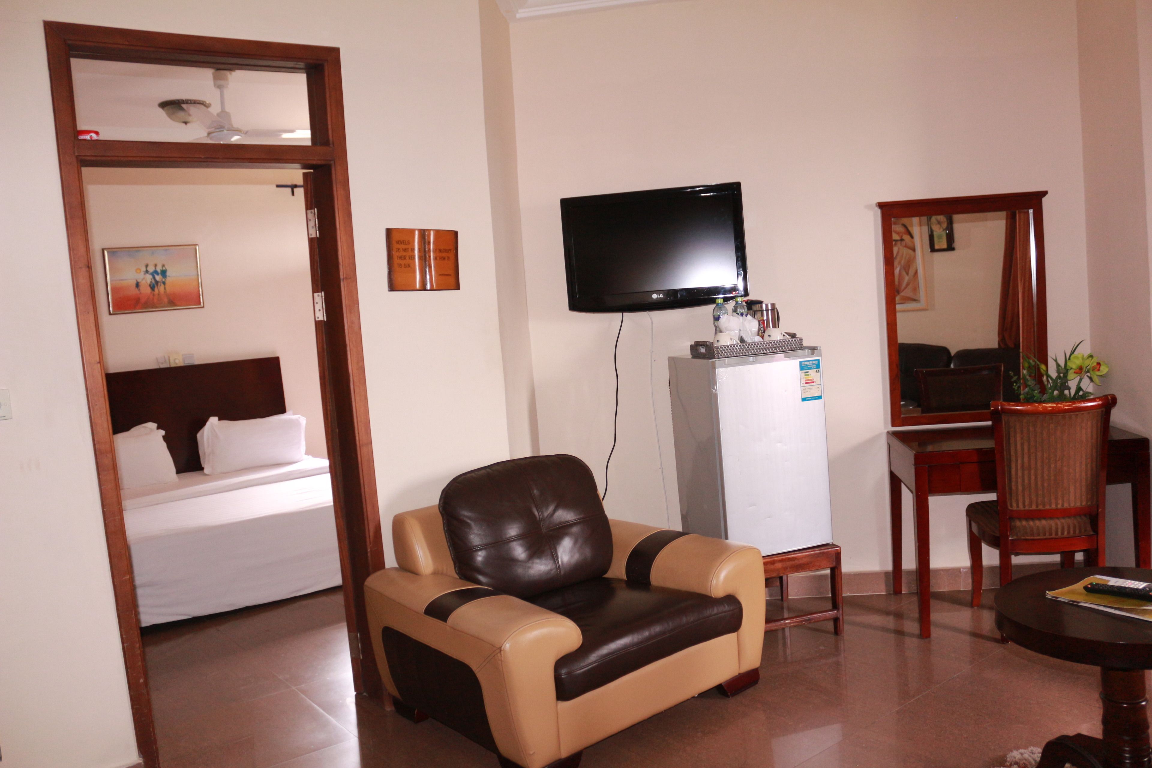 A hotel room with a bed, a leather armchair, a television, a refrigerator, a wooden table, and a mirror.