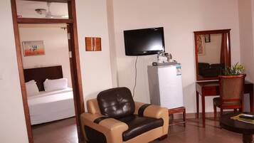 A hotel room with a bed, a leather armchair, a television, a refrigerator, a wooden table, and a mirror.