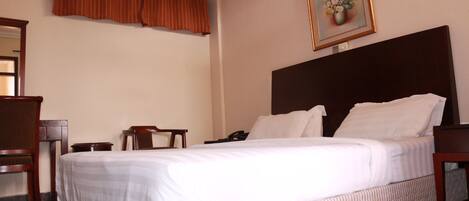 A hotel room with a large bed, a wooden headboard, a desk with a chair, and a painting on the wall.