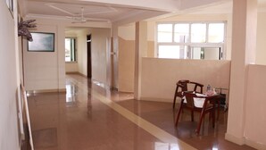 A spacious hallway with a polished floor, a dining area with wooden chairs, and a ceiling fan. - Windy Bay Guest House (Winneba)