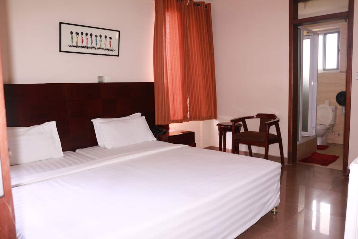 A hotel room with a large bed, a wooden headboard, a desk with a chair, and a bathroom visible through an open door.