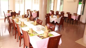 A spacious dining area with multiple tables and chairs, large windows, and an air conditioning unit on the wall. - Windy Bay Guest House (Winneba)