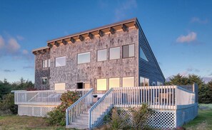 Une maison moderne à deux étages, dotée d’un toit en pente, de grandes fenêtres et d’une terrasse en bois avec des escaliers.