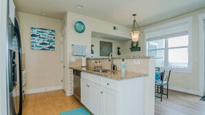 A kitchen with white cabinets, a granite countertop, a sink, and a dining area with a table and chairs. - Sea Pointe- The Perfect Beachfront Destination - Brand New Elevator (Galveston)