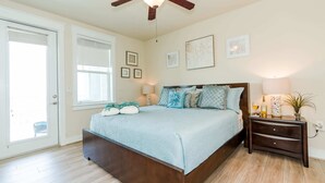 A bedroom with a bed, a nightstand, a ceiling fan, and a door. - Sea Pointe- The Perfect Beachfront Destination - Brand New Elevator (Galveston)