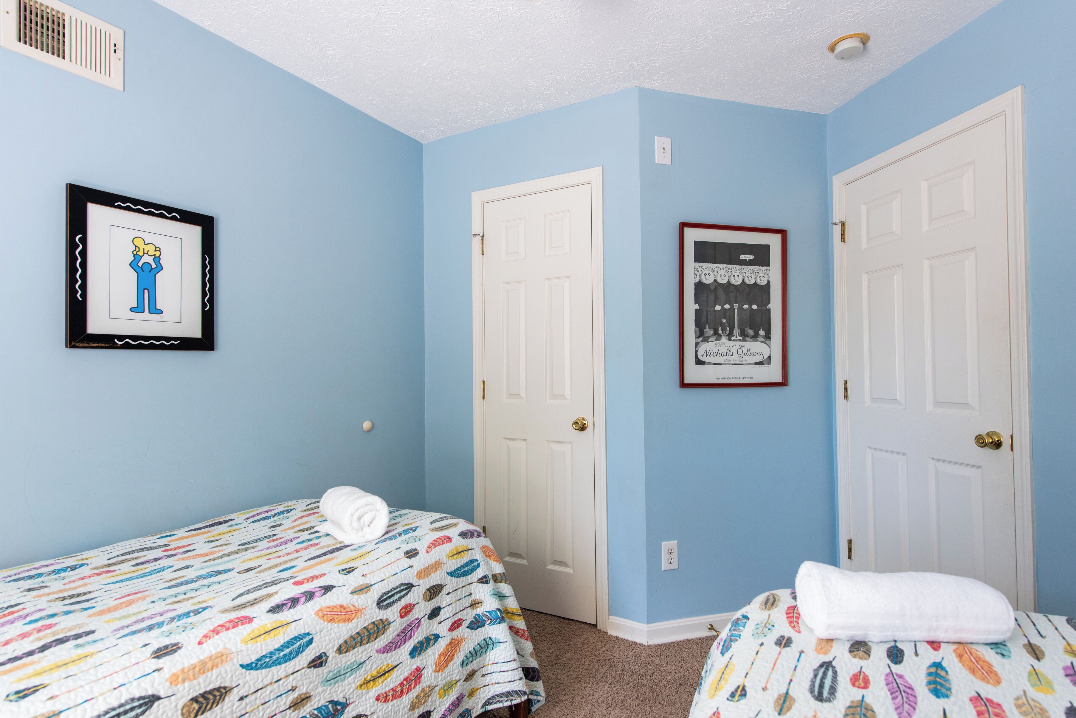 A bedroom with two beds, a white door, and a framed picture on the wall.