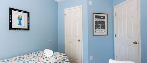 A bedroom with two beds, a white door, and a framed picture on the wall.