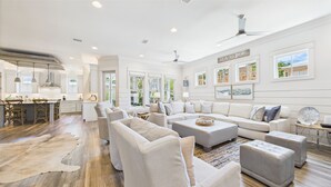 A spacious living room with a large sofa set, a dining area with a wooden table, and a kitchen with white cabinets. - 4 Bedroom Grayton Luxury-Elevator-Sleeps 12- Private beach access with set-up (Santa Rosa Beach)