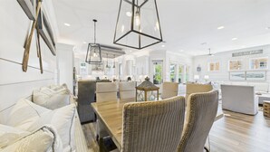 A modern living room with a large wooden dining table, wicker chairs, and a sofa with patterned cushions. - 4 Bedroom Grayton Luxury-Elevator-Sleeps 12- Private beach access with set-up (Santa Rosa Beach)