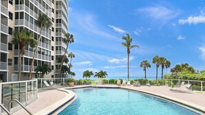 A swimming pool with a clear blue water, surrounded by a white fence, and palm trees in the background. - Crystal Sands Tower Unit 502 - Beachfront (SARASOTA)