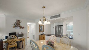 A modern kitchen with a stainless steel refrigerator, a dining area with a marble table, and a decorative wall piece. - Crystal Sands Tower Unit 305 - Beachfront (Sarasota)