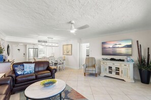 A spacious living room with a leather sofa, a dining area, a ceiling fan, and a large painting on the wall.