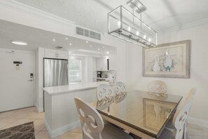 A modern kitchen with a glass dining table, white chairs, a stainless steel refrigerator, and a pendant light fixture.