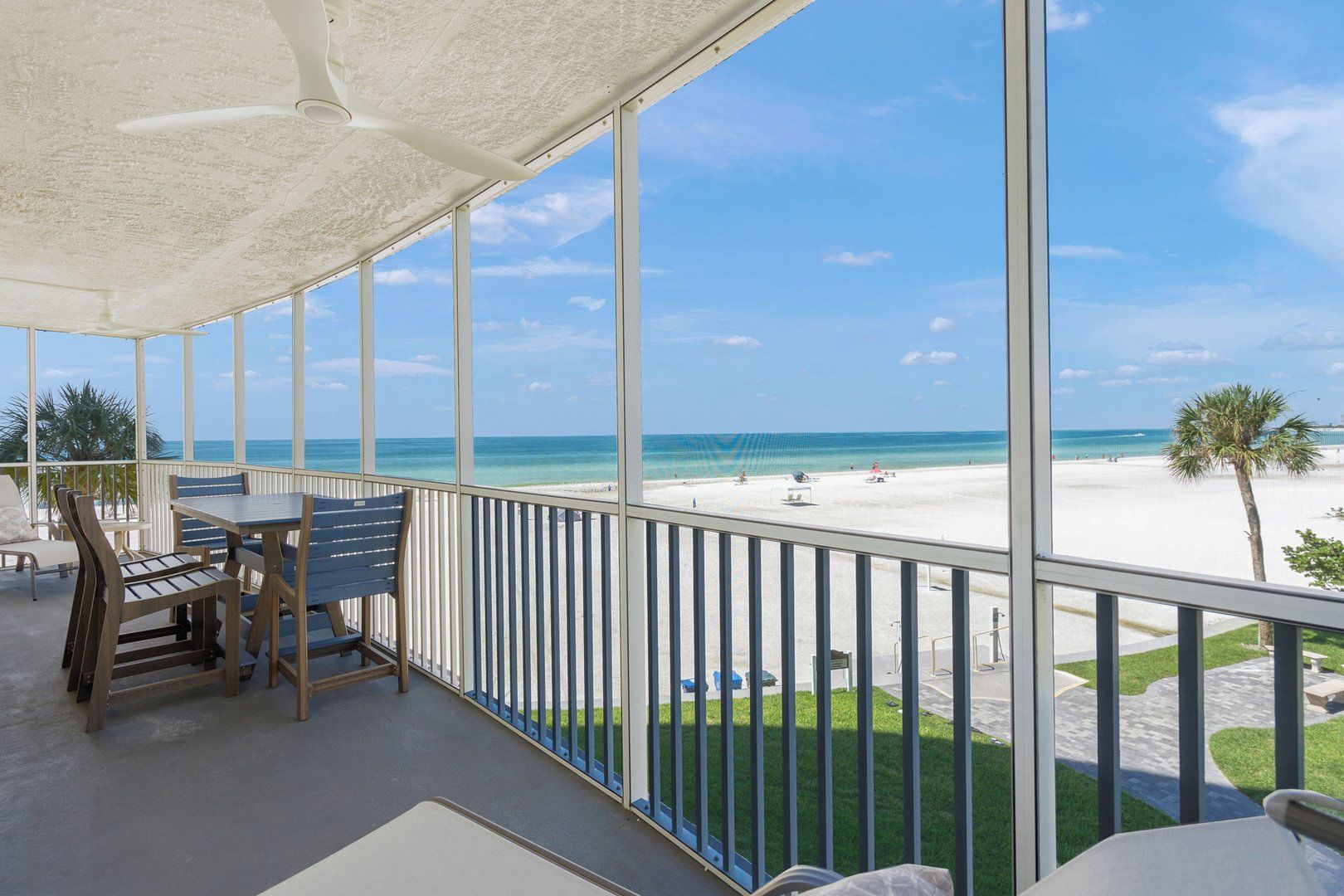 A balcony with a view of a beach, a table, and chairs.