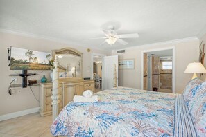 Ein Schlafzimmer mit Bett, Kommode, Schminktisch, Deckenventilator und Fernseher.