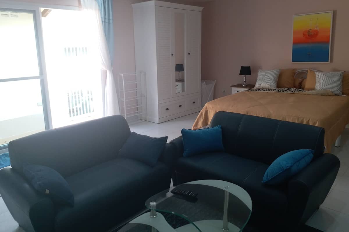 A modern bedroom with a bed, two sofas, a glass coffee table, a wardrobe, and a painting on the wall.