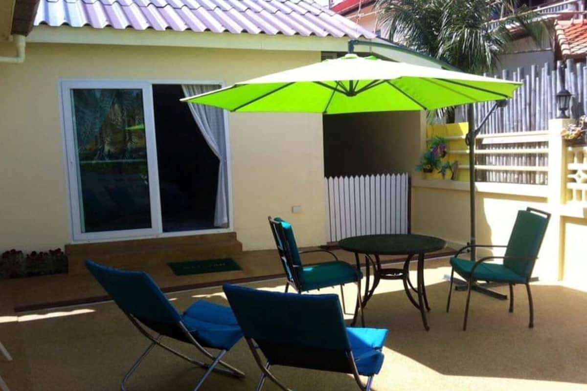 An outdoor patio with a table and four chairs, a green umbrella, and a sliding glass door.