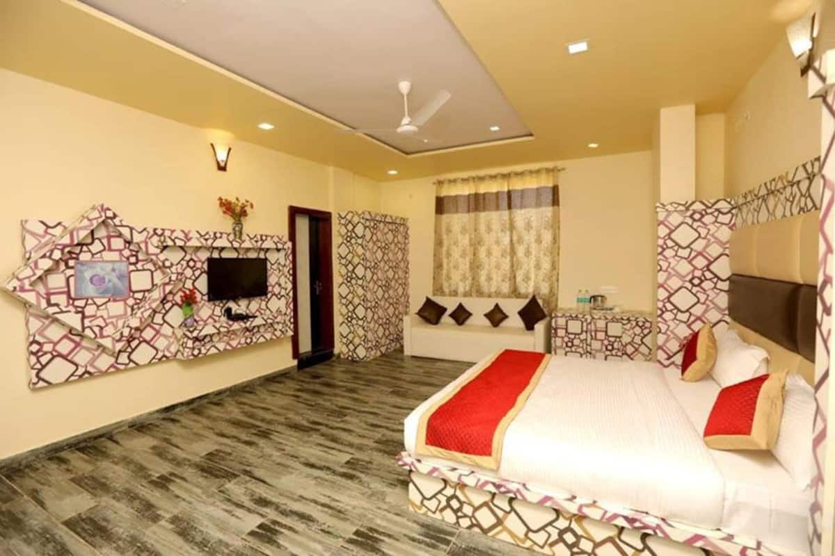 Une chambre d’hôtel avec un lit, un téléviseur fixé au mur, un ventilateur de plafond et des murs à motifs.