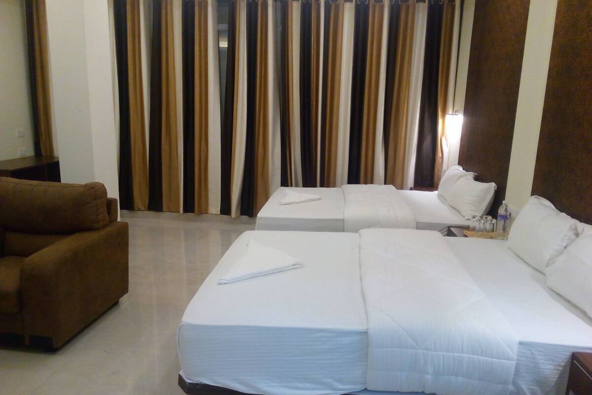 A hotel room with two beds, a brown armchair, and a curtain with a striped pattern.