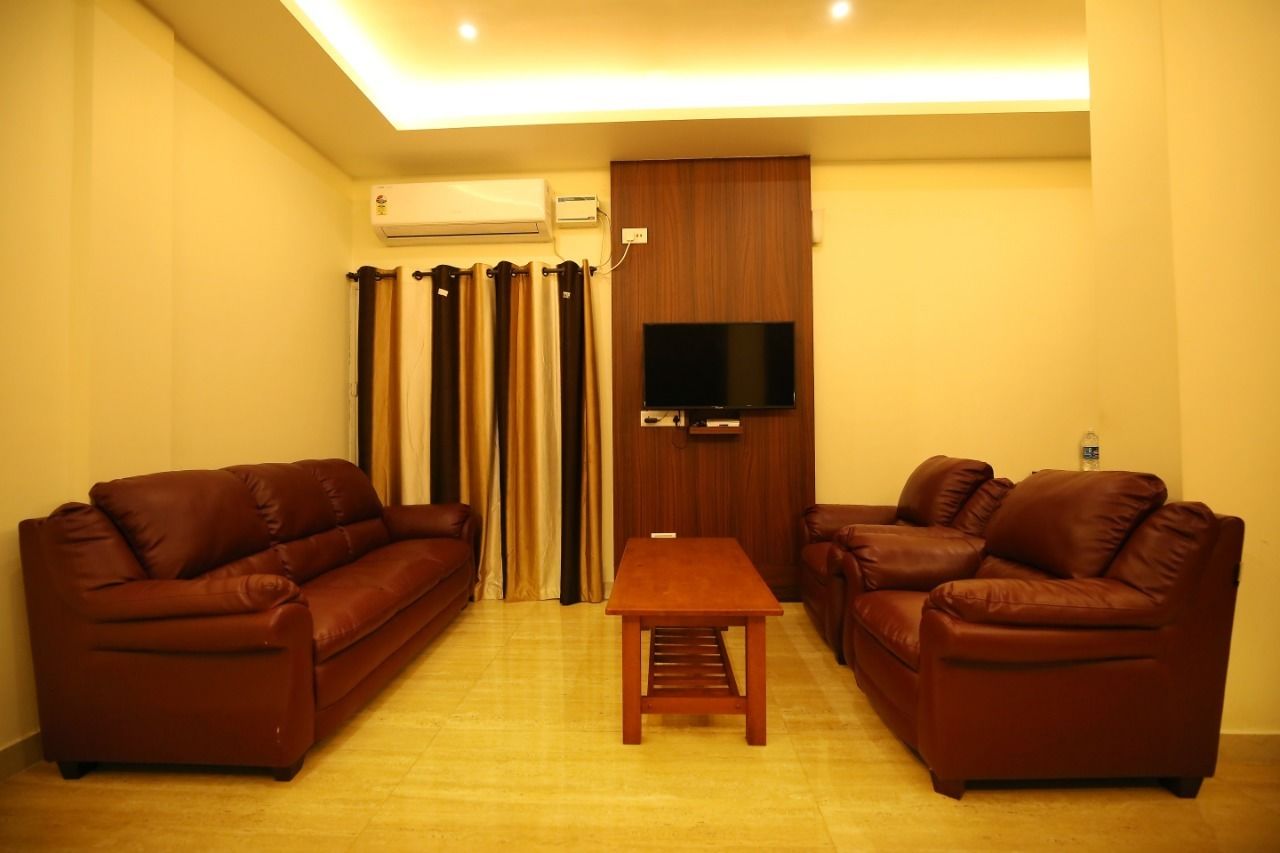 A living room with two brown leather sofas, a wooden coffee table, a flat-screen TV mounted on a wooden panel, and an air conditioning unit on the wall.