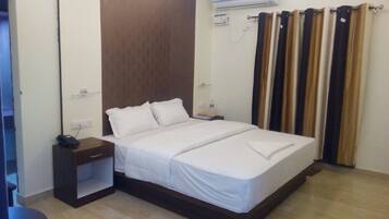 Habitación de hotel con cama, mesita de noche, una silla y ventana con cortinas.