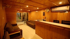 Interior de madeira com balcão de recepção, um relógio e placa indicativa da recepção.