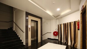 Um saguão de hotel moderno com escadas, elevador e uma fileira de cortinas.