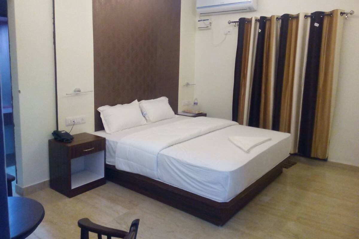 A hotel room with a bed, a nightstand, a chair, and a curtain.