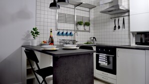 Cozinha moderna com ilha central, luminárias pendentes pretas, exaustor de aço inoxidável e paredes com azulejos brancos.