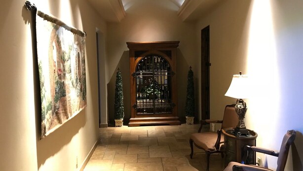 Un couloir avec une porte en bois, une chaise, une lampe et un tableau accroché au mur.