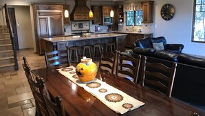 Une cuisine spacieuse dotée de meubles en bois, d’un îlot central, de luminaires suspendus et d’un coin repas avec une table dressée pour quatre personnes.
