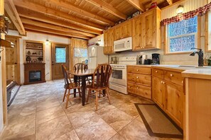 A wooden interior with a dining table, chairs, a fireplace, a kitchen with wooden cabinets, a microwave, and a stove.