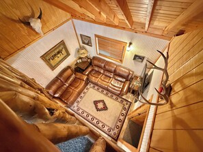 Un interno accogliente di una baita con un divano in pelle, un tappeto decorato, pareti in legno e decorazioni con corna di cervo.