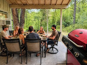 Un'area pranzo all'aperto coperta, con una griglia, circondata da alberi.