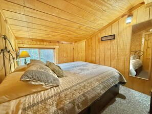 A wooden cabin bedroom with a bed, a nightstand, a lamp, and a window.