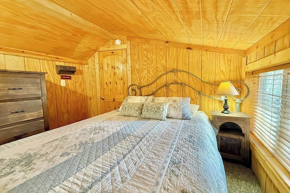 Une chambre à coucher aux murs lambrissés, avec un lit, une commode et une lampe.