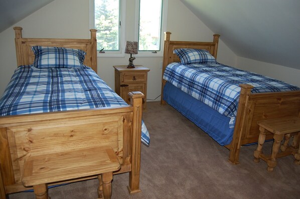 Two wooden beds with blue and white checkered bedding, a small wooden nightstand, and a window with a view of trees.