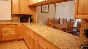 A kitchen with wooden cabinets, granite countertops, a microwave, and a dining area with wooden chairs and a table.