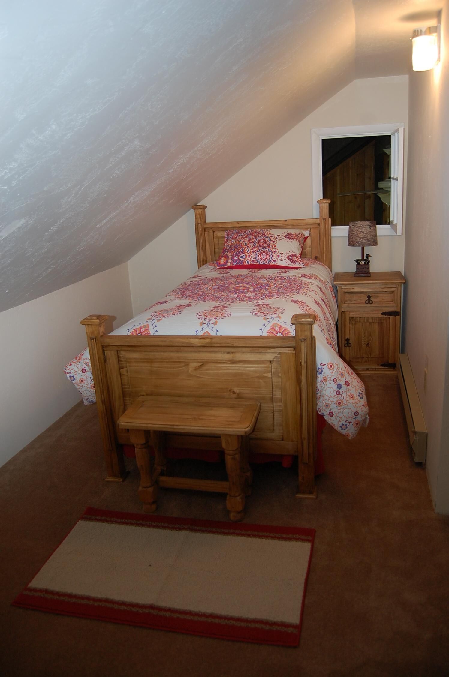 A bedroom with a wooden bed, a bedside table, a nightstand, a mirror, and a window.
