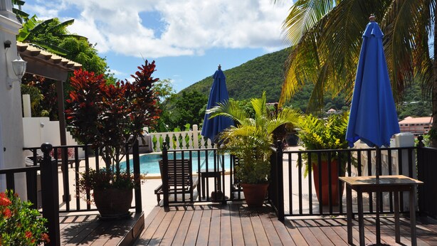 Une terrasse en bois avec une piscine, des plantes en pot et des parasols bleus.