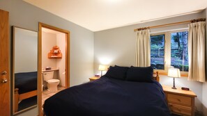 A bedroom with a bed, bedside tables, a window with curtains, a mirror, and a view of the outdoors.