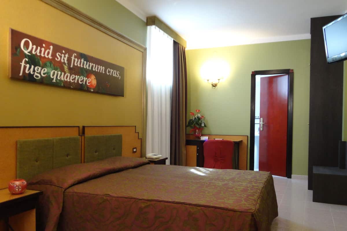 Habitación de hotel con cama, escritorio, silla, televisión y una pared con un letrero.