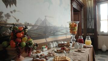 A breakfast buffet with a variety of fruits, pastries, and beverages on a table with a view of a mountain landscape.